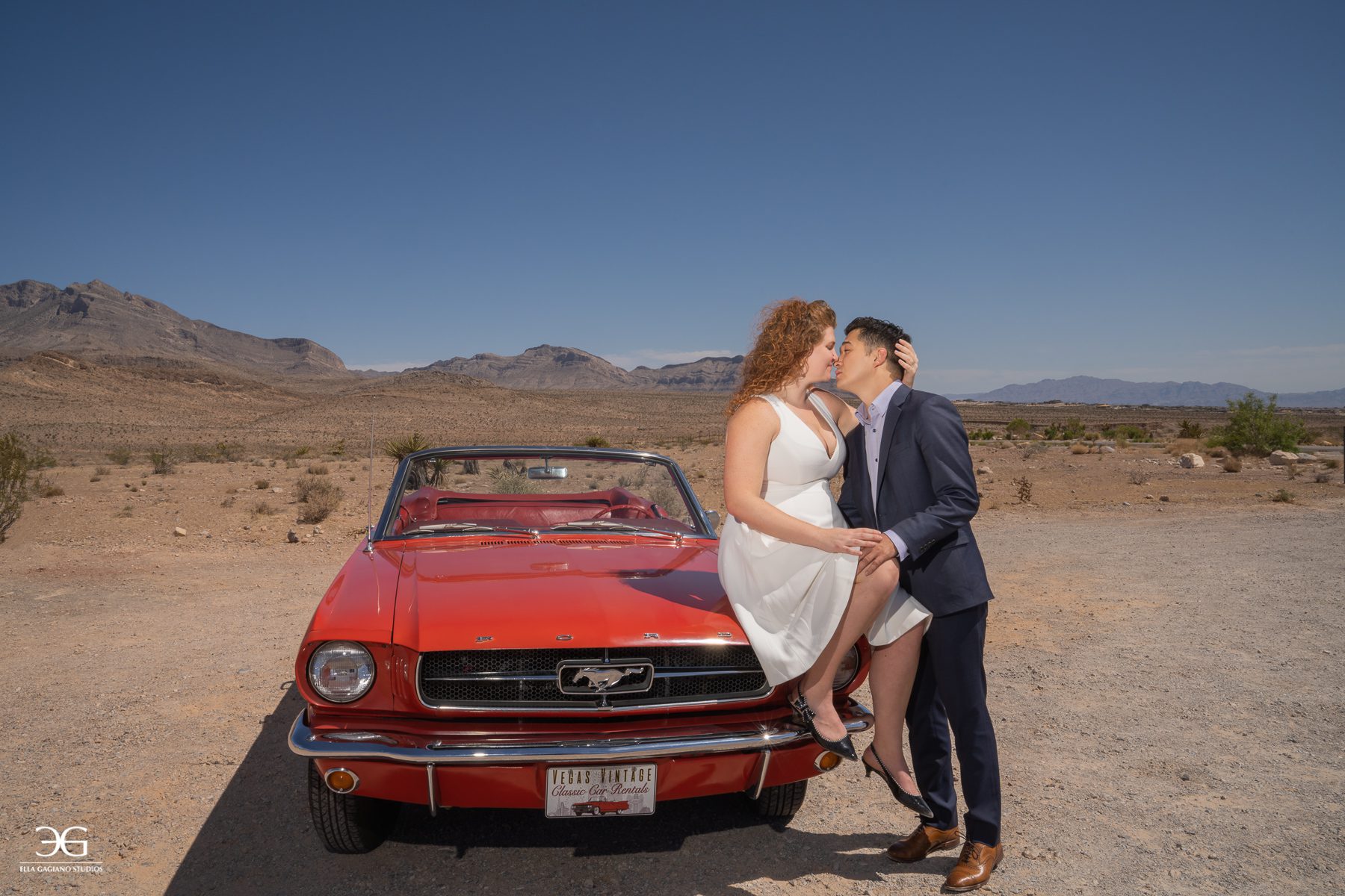 couple kissing on red ford mustang in desert engagement photoshoot