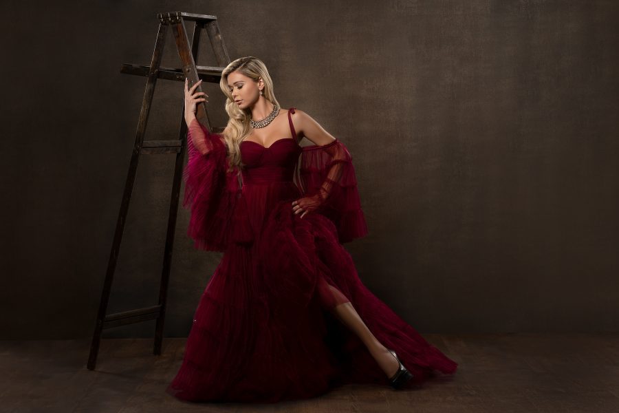 Strong woman in burgundy dress near ladder, glamour photoshoot