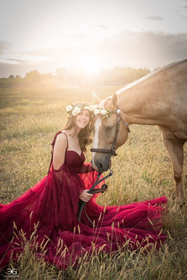 Teen girl in a burgundy gown sharing a quiet moment with her horse in a field