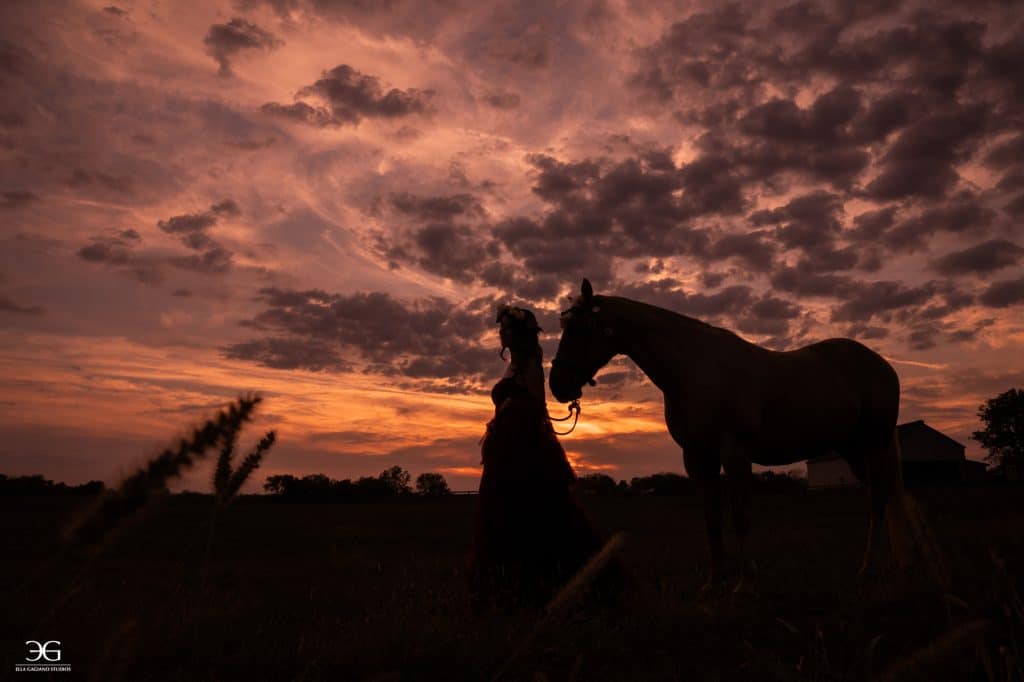Silhouette of a teen equestrian and her horse against a dramatic sunset