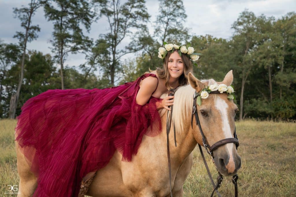 Teen girl in a flowing burgundy dress leaning across her horse in a field
