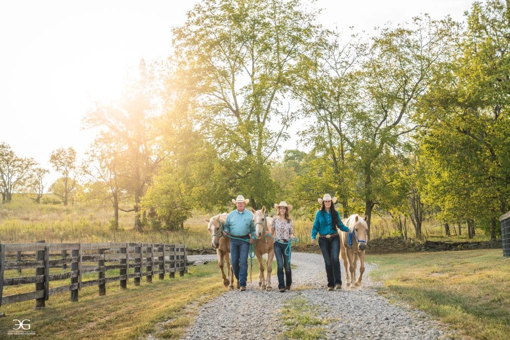 Teen girl and two mentors walking with three horses along a Kentucky farm lane