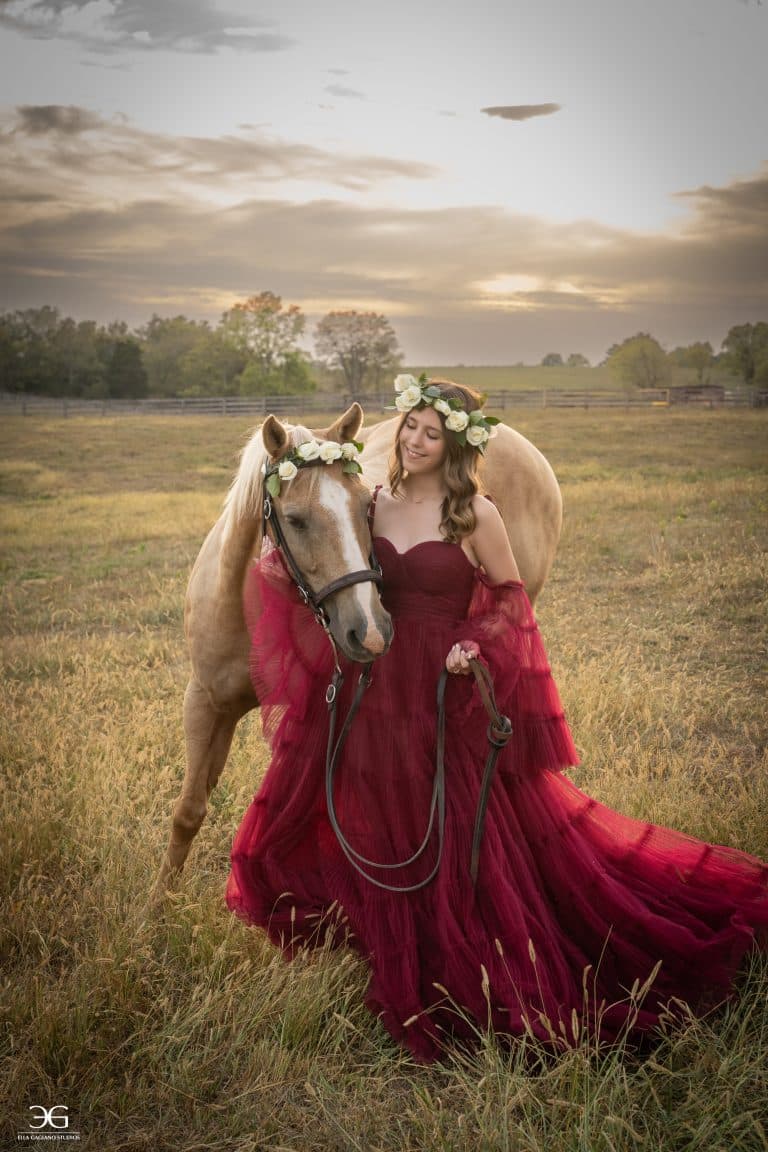 Teen equestrian in a flowing burgundy gown standing beside her horse