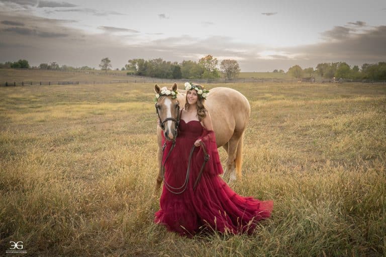 Teen equestrian in a burgundy dress standing beside her horse in a Kentucky field