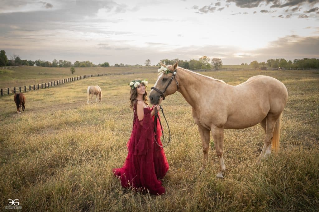 Teen girl in a burgundy dress standing with her horse in a wide Kentucky pasture